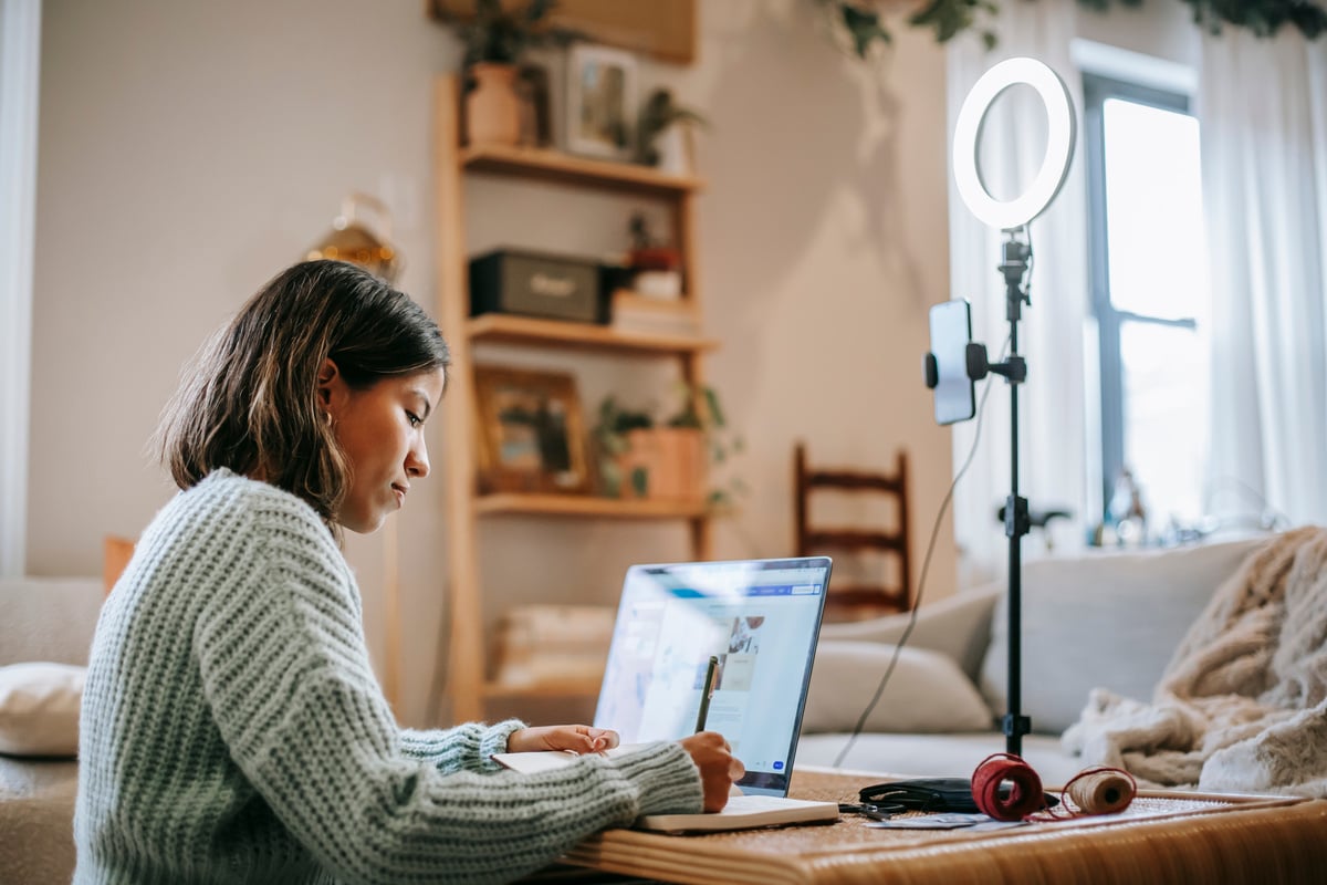 Woman writing at table with laptop and ring lamp